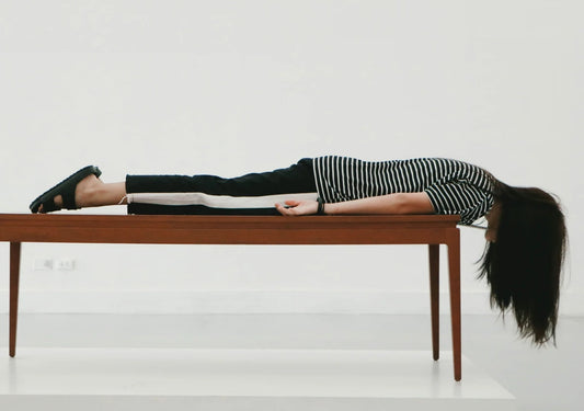 A woman lying face down across a wooden bench in an empty white room