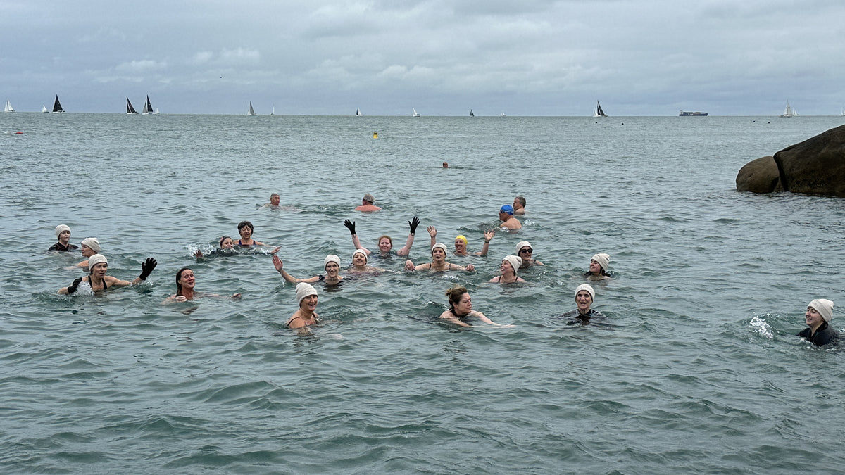 SISTERLY Circle sea swim: a group of women waving from the water in white swim caps